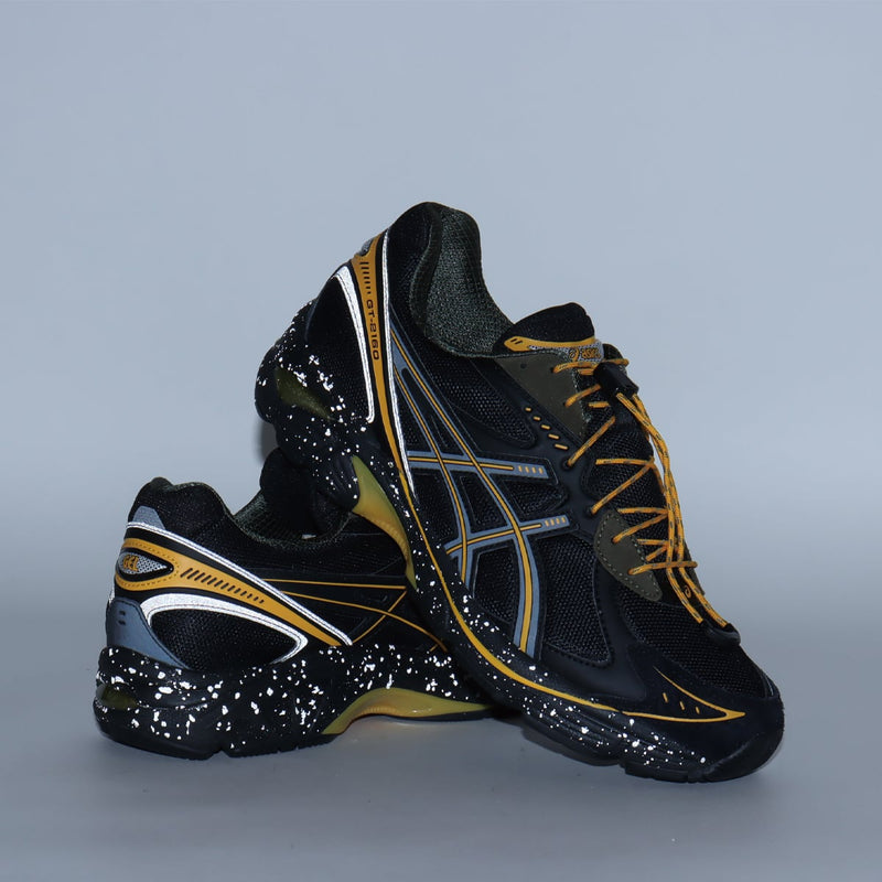 atmos x GRIPSWANY x ASICS SportStyle GT-2160 sneakers featuring a black upper with Swany Yellow ASICS stripes, drawstring laces, reflective details, and a duck camo insole.