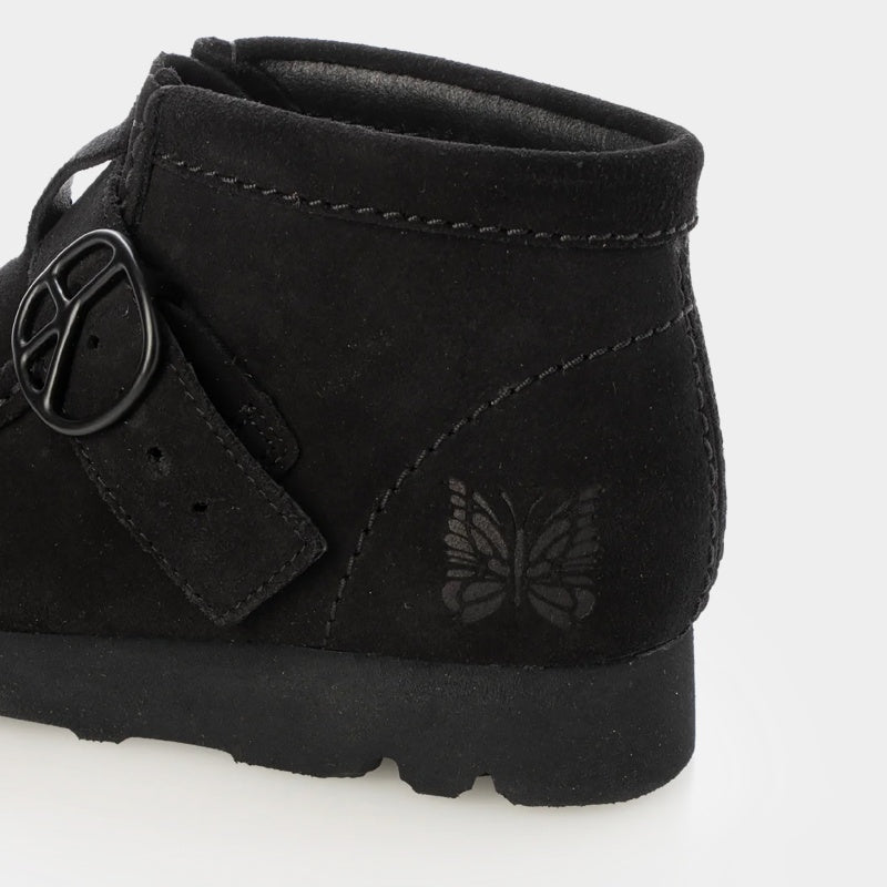 Clarks x Needles Wallabee boot featuring suede upper, debossed butterfly detail, and metal peace sign buckle on adjustable strap.