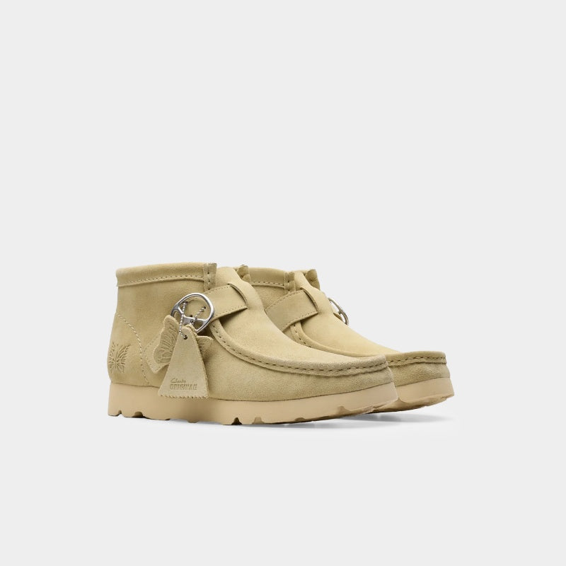 Clarks x Needles Wallabee boot featuring suede upper, debossed butterfly detail, and metal peace sign buckle on adjustable strap.