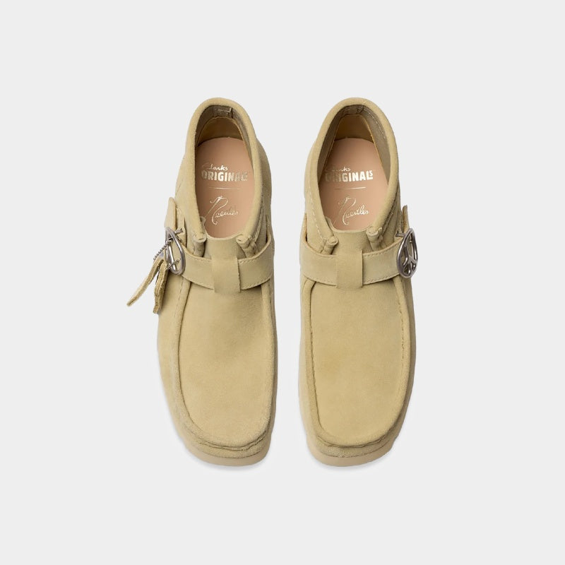 Clarks x Needles Wallabee boot featuring suede upper, debossed butterfly detail, and metal peace sign buckle on adjustable strap.