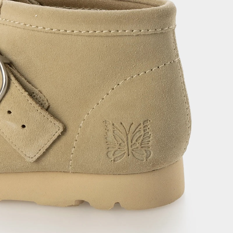 Clarks x Needles Wallabee boot featuring suede upper, debossed butterfly detail, and metal peace sign buckle on adjustable strap.
