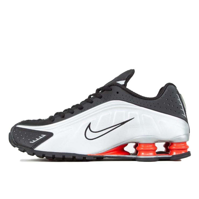 Shox R4 sneaker in black, metallic silver, and max orange, featuring a super-soft synthetic upper with fluid waves and laser perforations, and four compression columns for enhanced stability and bounce.
