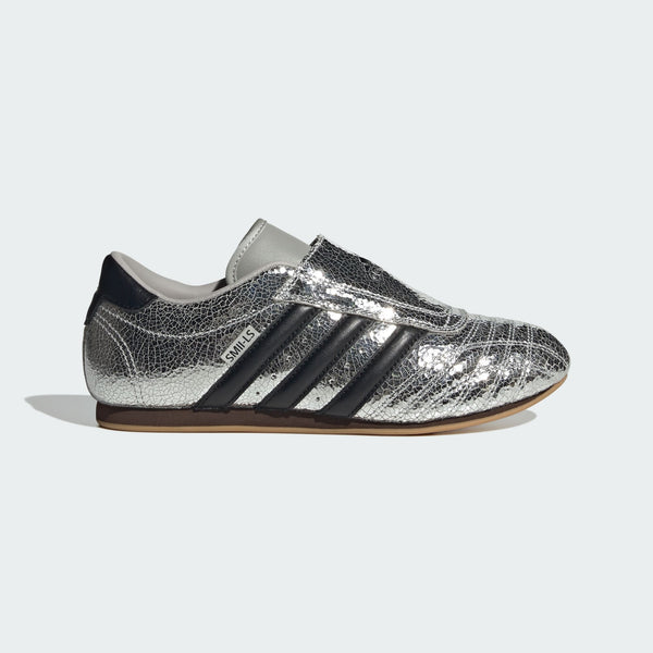 adidas Taekwondo trainers with a cracked metallic leather upper, slip-on design, and low-profile rubber outsole for a sleek, streetwear-inspired look.