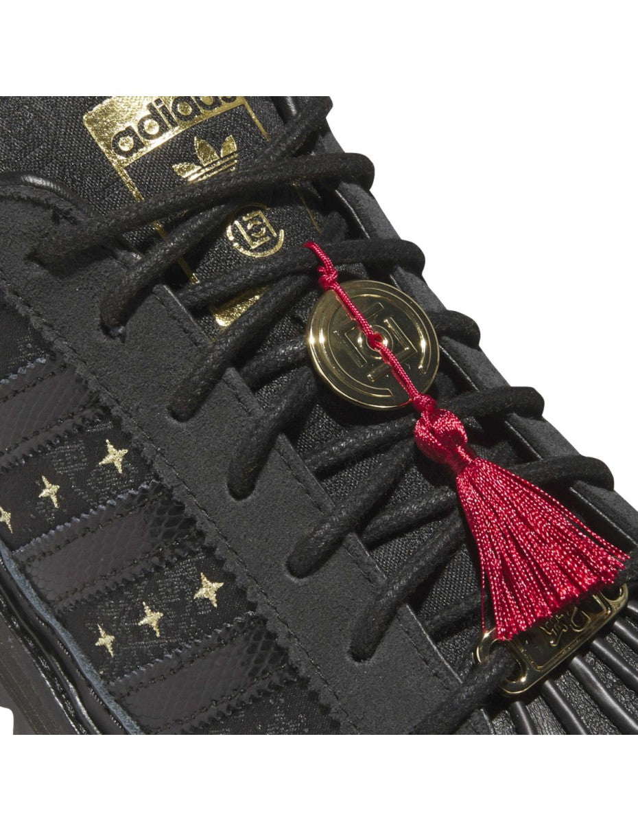 adidas Superstar x CLOT sneaker with snakeskin-patterned 3-Stripes, monogram print, gold details, red string accents, and a rippled outsole for a bold Lunar New Year tribute.
