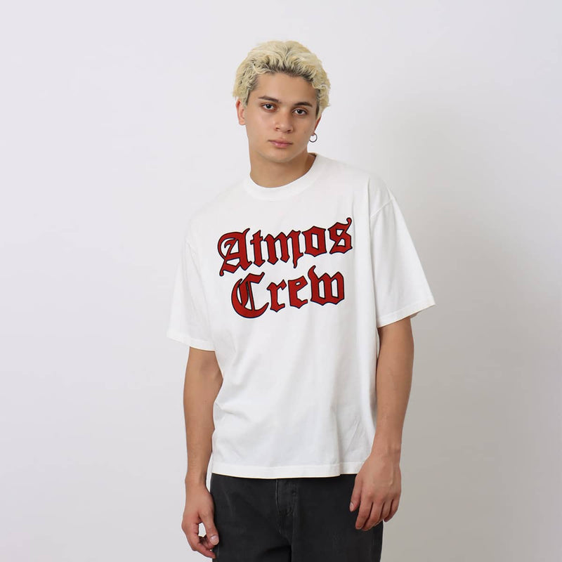 Atmos short-sleeved T-shirt with Old English-style Atmos Crew motif on the front and blue pistag on the left hem, crafted from soft, smooth fabric. Model height 180cm, wearing size L.