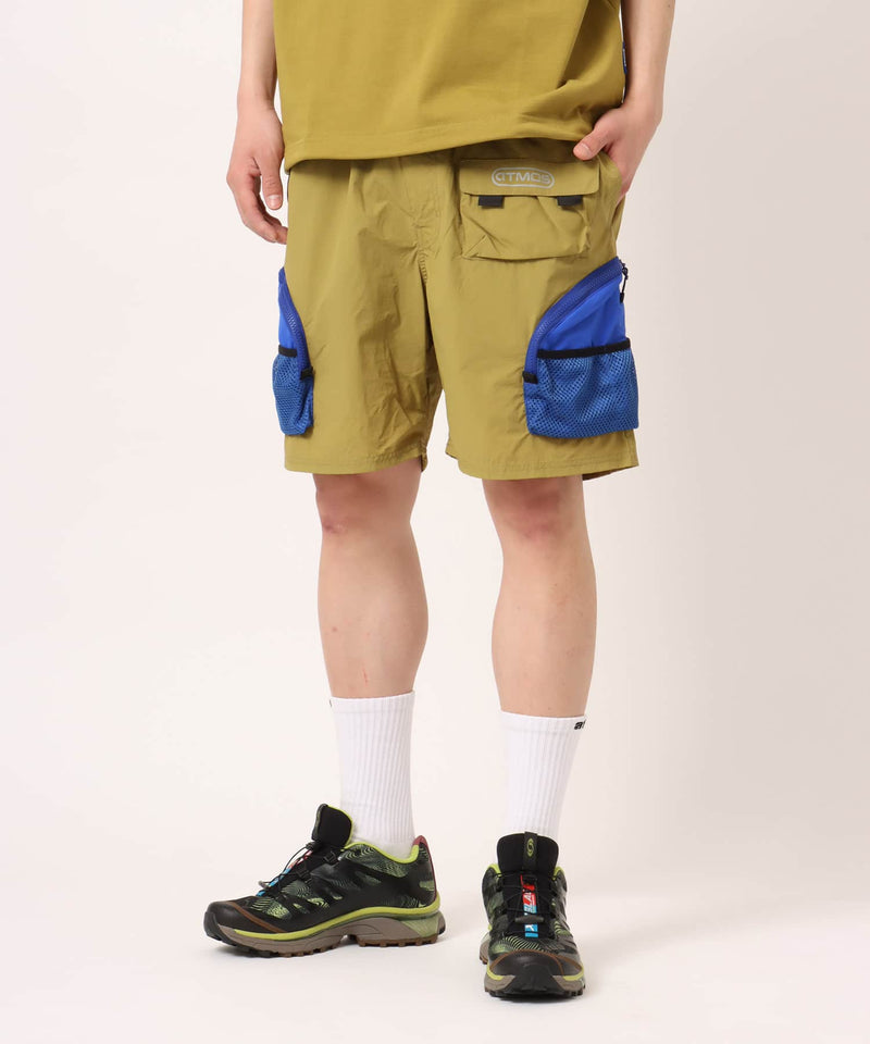 Model wearing functional cargo shorts with mesh and flap pockets in durable cotton fabric.