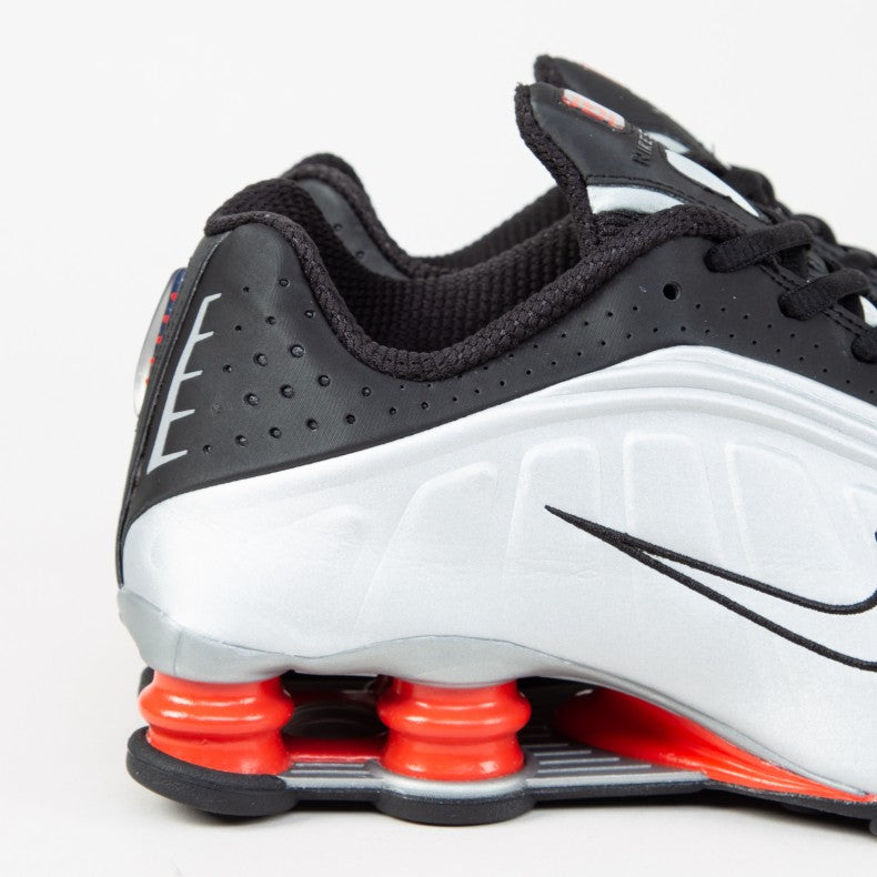 Shox R4 sneaker in black, metallic silver, and max orange, featuring a super-soft synthetic upper with fluid waves and laser perforations, and four compression columns for enhanced stability and bounce.



