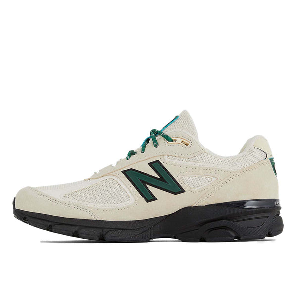 This iconic running shoe showcases the triumphant return of the New Balance 990 v4 after an 8-year hiatus. It features a light beige mesh upper adorned with suede overlays, complemented by black and dark green accents. 