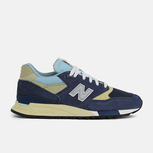 New Balance 998 Made in USA sneakers in navy with chrome blue accents, featuring ABZORB cushioning and premium suede, mesh, and hairy suede construction.